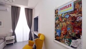 Una habitación con un sillón amarillo, una mesita de noche blanca, una cama y un cartel grande de Los Beatles, 'Yellow Submarine', en la pared.
