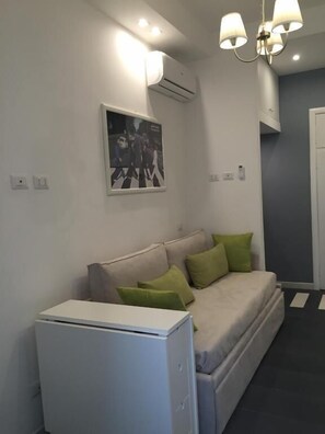 A modern, compact living space with a sofa bed, a small white cabinet, and a wall-mounted air conditioner. - Rome Together Guest House (Rome)