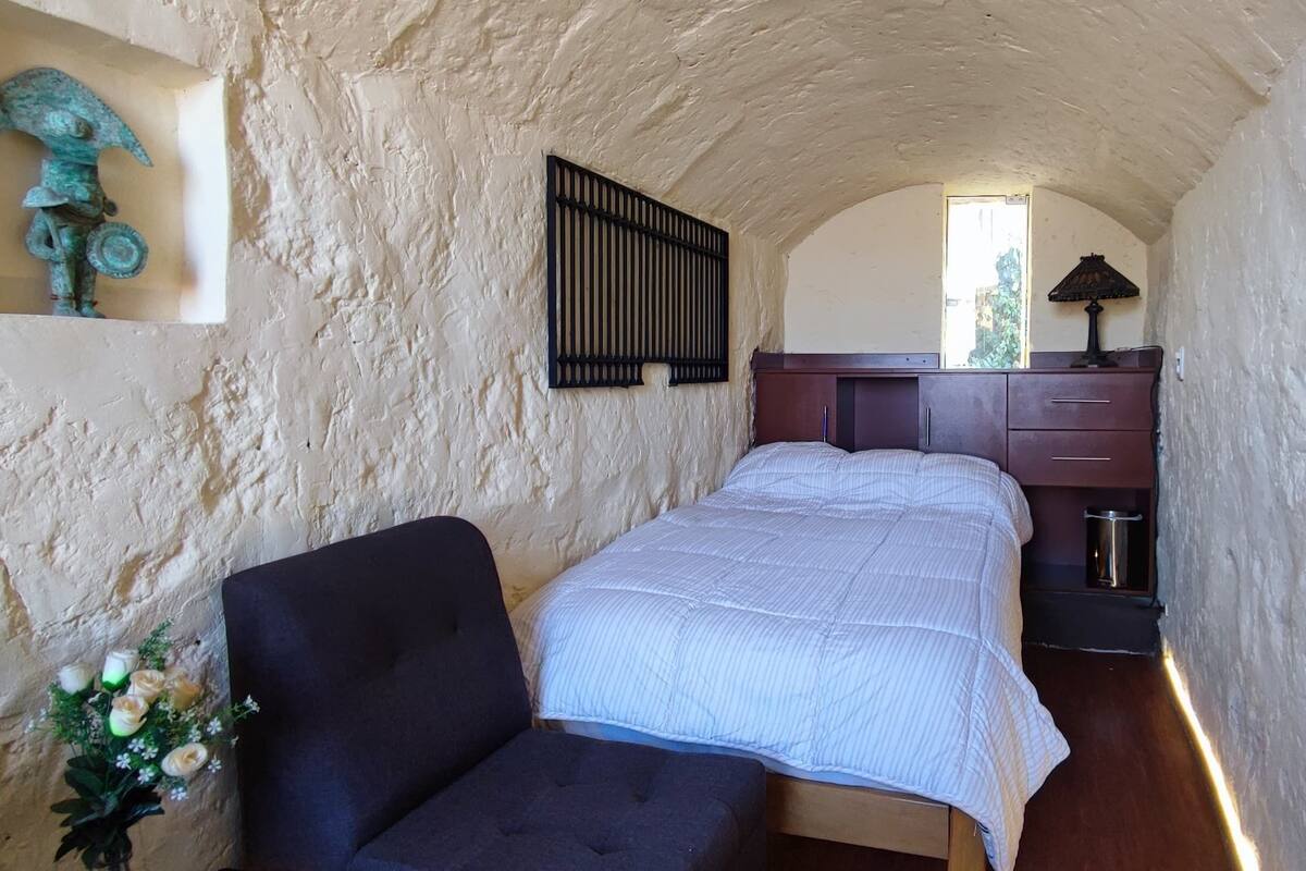 Une petite pièce comprenant un lit, une chaise, une petite table et un objet décoratif accroché au mur.