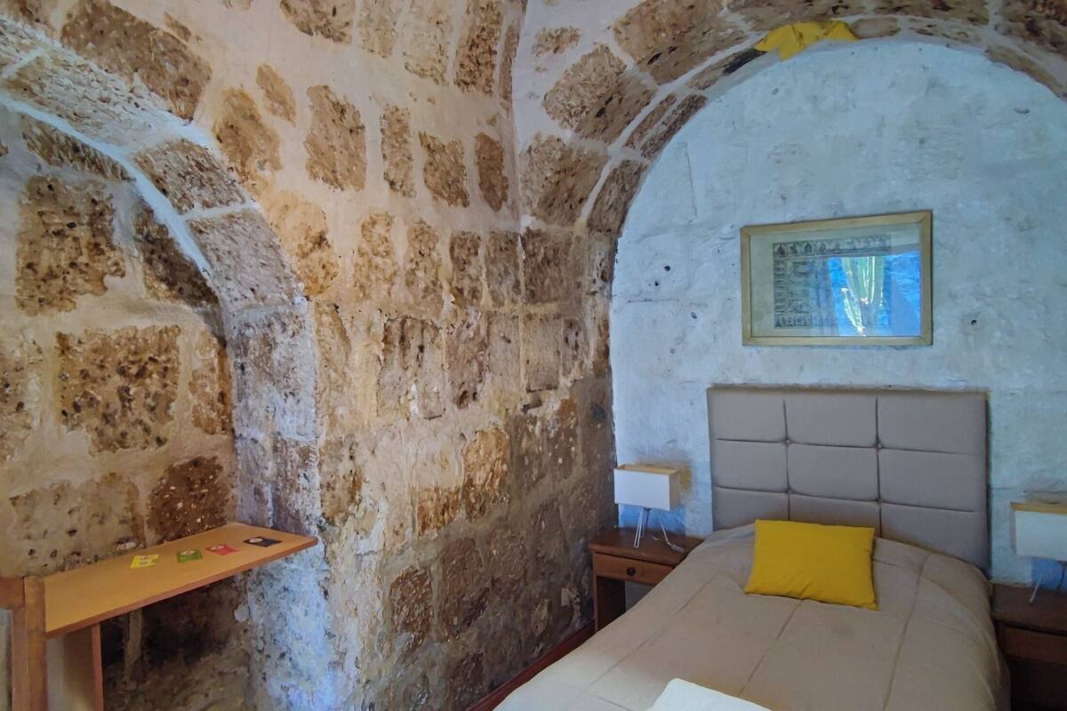 Une pièce aux murs de pierre, avec un lit, une table de chevet, une petite table et un miroir.
