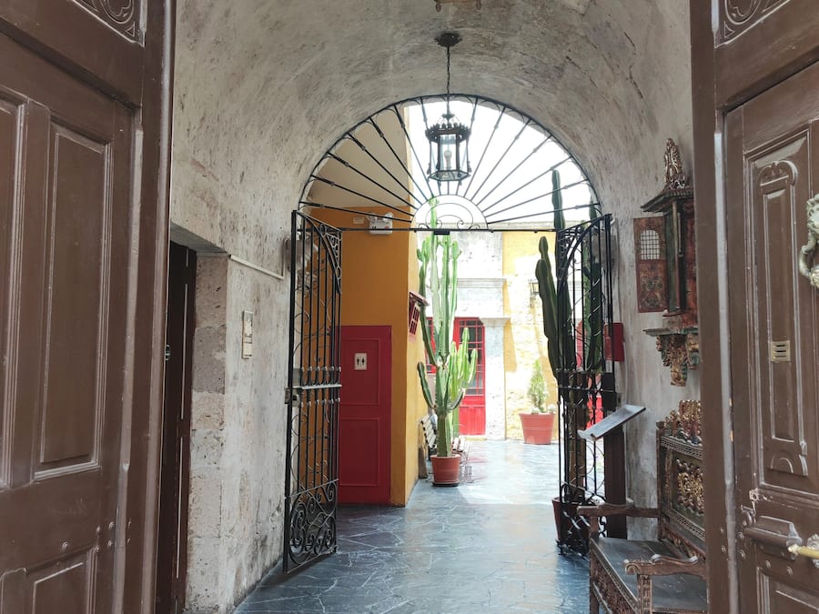 Un pasillo arqueado con suelo de baldosas, una puerta roja y una planta de cactus.