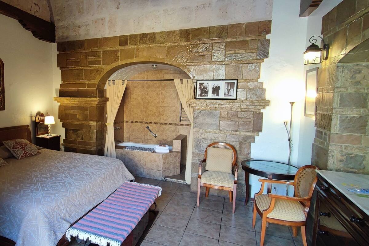 Une chambre à coucher avec un lit, une chaise en bois, une petite table, une cheminée en pierre et une porte rouge.