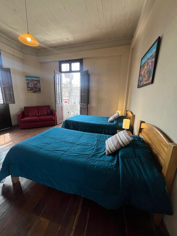 A room with two beds, a red sofa, a wooden ceiling, and a painting on the wall. - Flying Dog Hostels Arequipa (Arequipa)