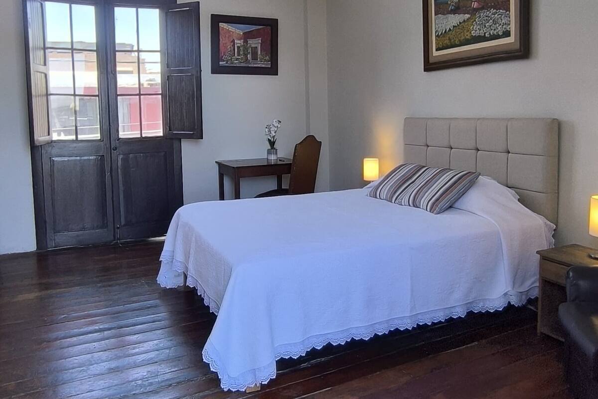 Une chambre avec un grand lit, un plancher en bois, un bureau et une chaise.