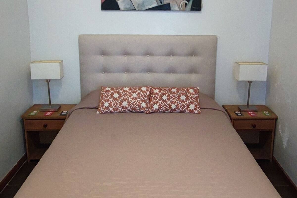 Une chambre à coucher avec un grand lit, une tête de lit capitonnée, deux tables de chevet avec des lampes et un tableau au mur.