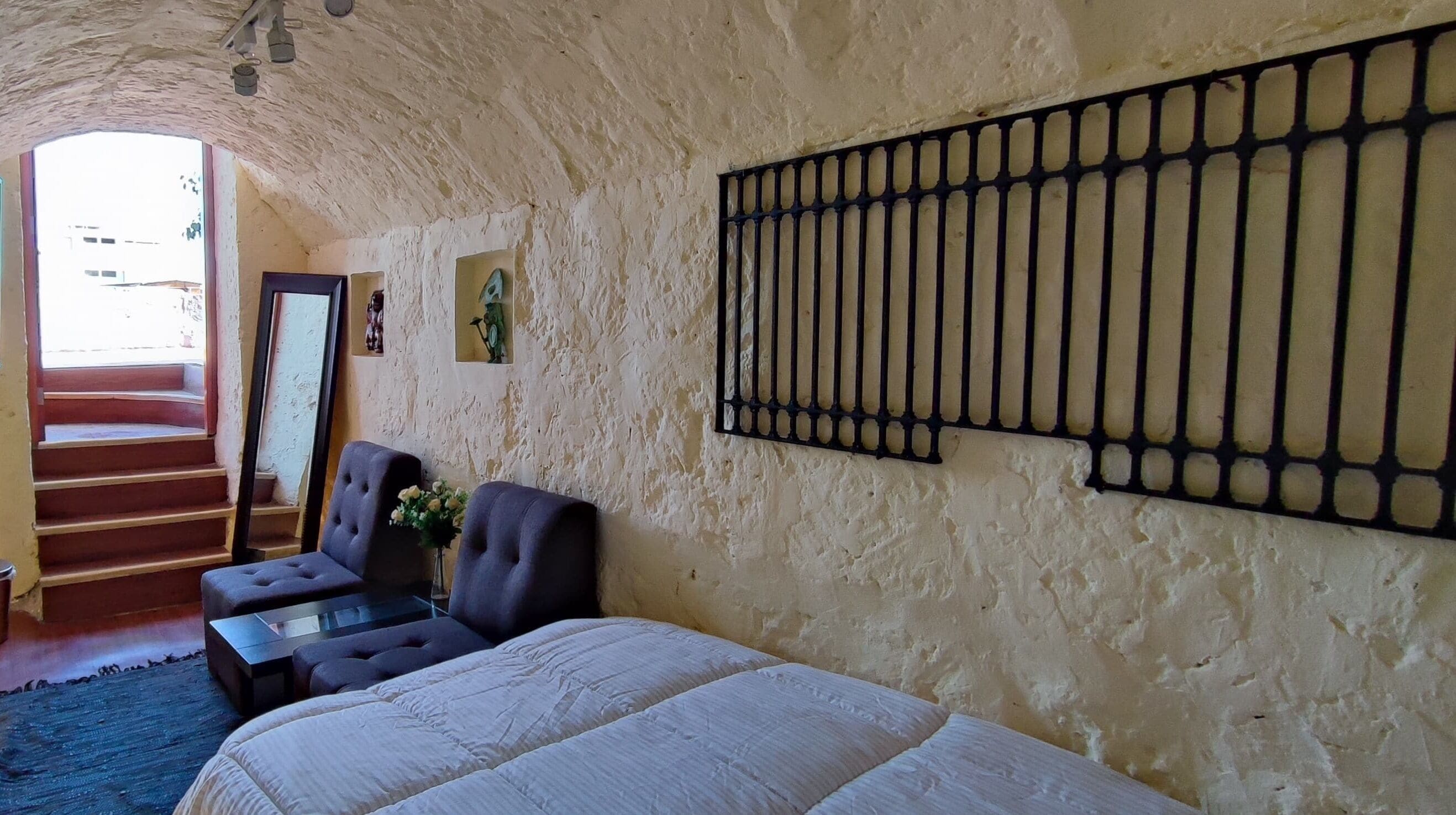 A bedroom with a bed, two armchairs, a small table, and a decorative wall piece.