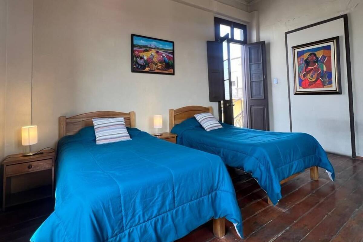 Une chambre avec deux lits, des têtes de lit en bois, un plancher en bois, un luminaire au plafond et deux tableaux accrochés aux murs.
