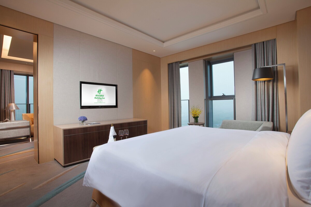Une chambre d’hôtel avec un grand lit, un bureau avec une chaise, un téléviseur fixé au mur et une fenêtre avec des rideaux.