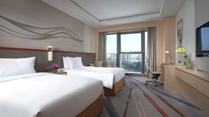 Une chambre d’hôtel avec deux lits, un bureau, une chaise et une grande fenêtre donnant sur la ville.