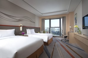A hotel room with two beds, a desk, a chair, and a large window offering a city view.