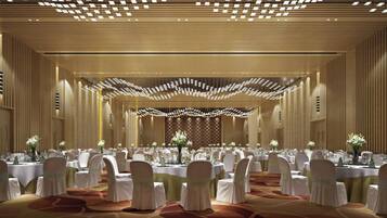 A banquet hall with round tables, white chairs, and a decorative ceiling.