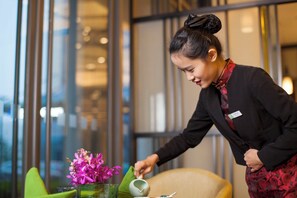 A person in a black outfit with a name tag, pouring water into a glass on a table with a vase of pink flowers.