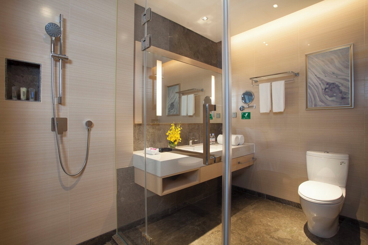 Une salle de bain moderne dotée d’une douche à parois de verre, d’un meuble-lavabo avec un miroir, de toilettes et d’une œuvre d’art encadrée accrochée au mur.