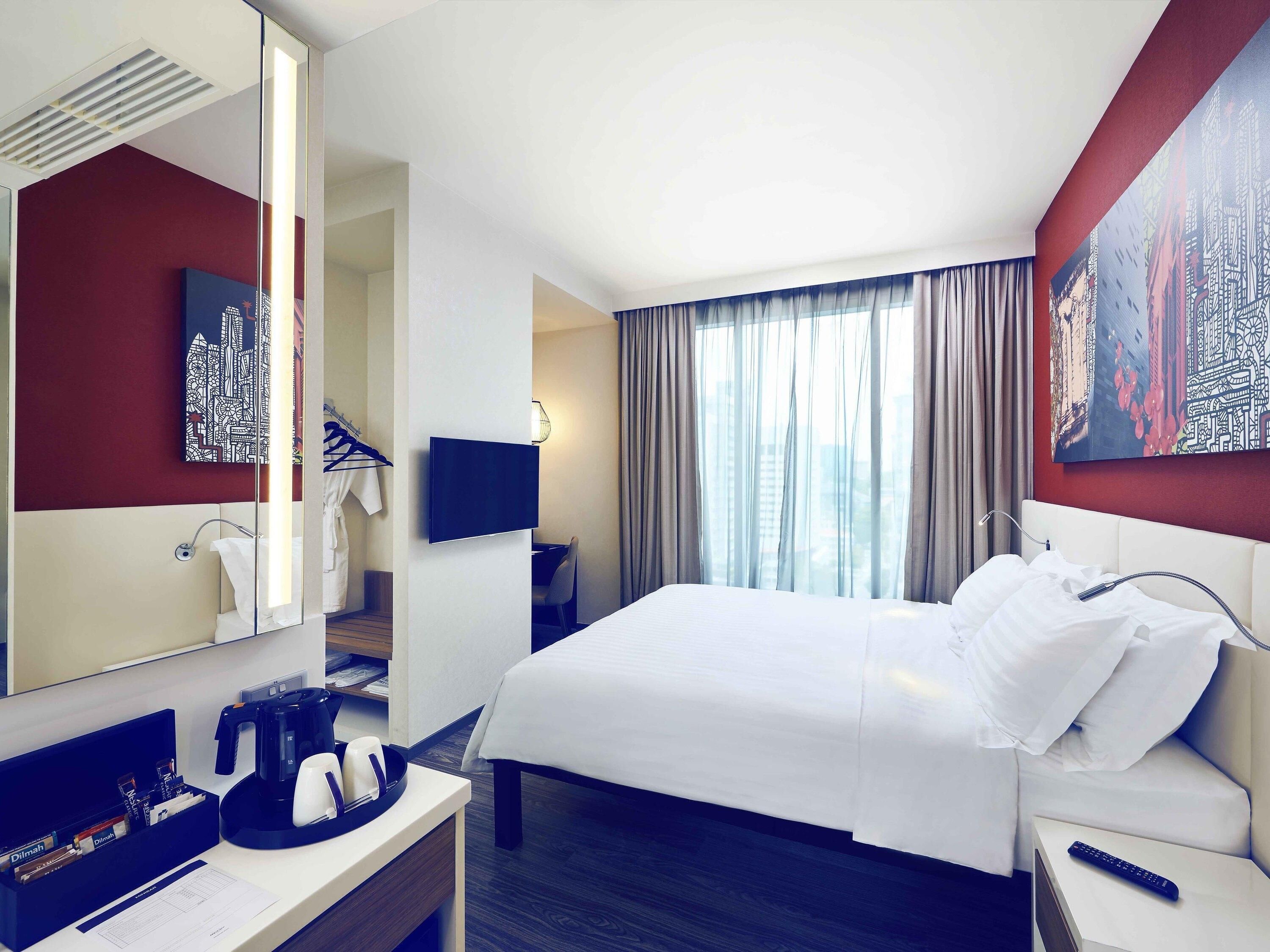 Una habitación de hotel con una cama, un escritorio con cafetera, un televisor y un ventanal con cortinas.