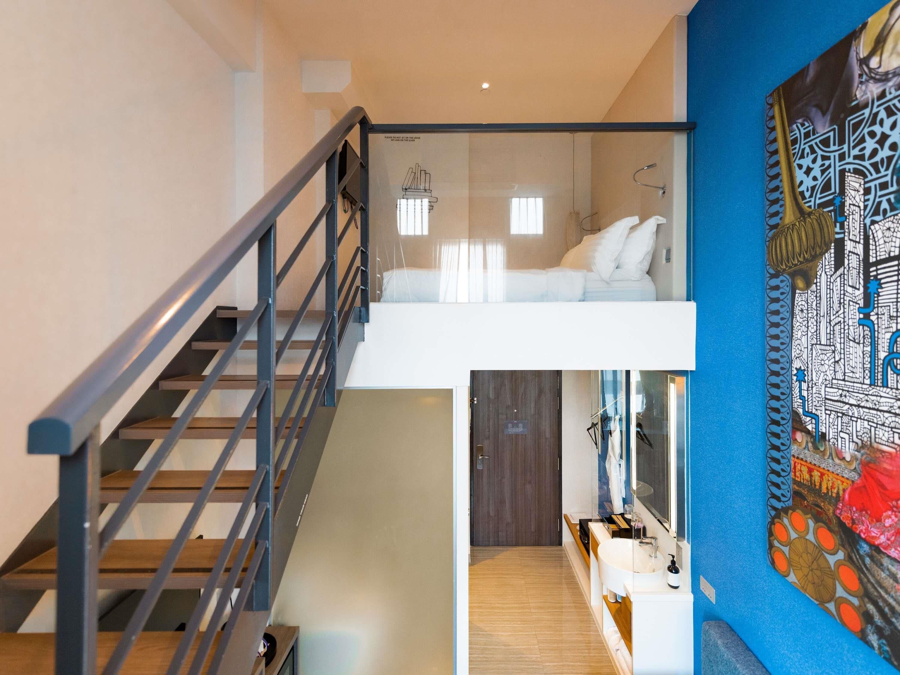 Un interior moderno con una escalera, un dormitorio en entrepiso, un baño con un espejo grande y una pared decorada con un mural detallado.