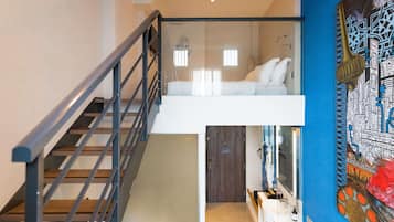 Un interior moderno con una escalera, un dormitorio en entrepiso, un baño con un espejo grande y una pared decorada con un mural detallado.