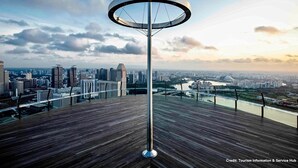 Una torre de observación moderna con una plataforma circular de vistas panorámicas, con vistas a un paisaje urbano de rascacielos y un río.
