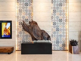 A reception area with a wooden bench, a large wooden sculpture, and patterned tile walls.