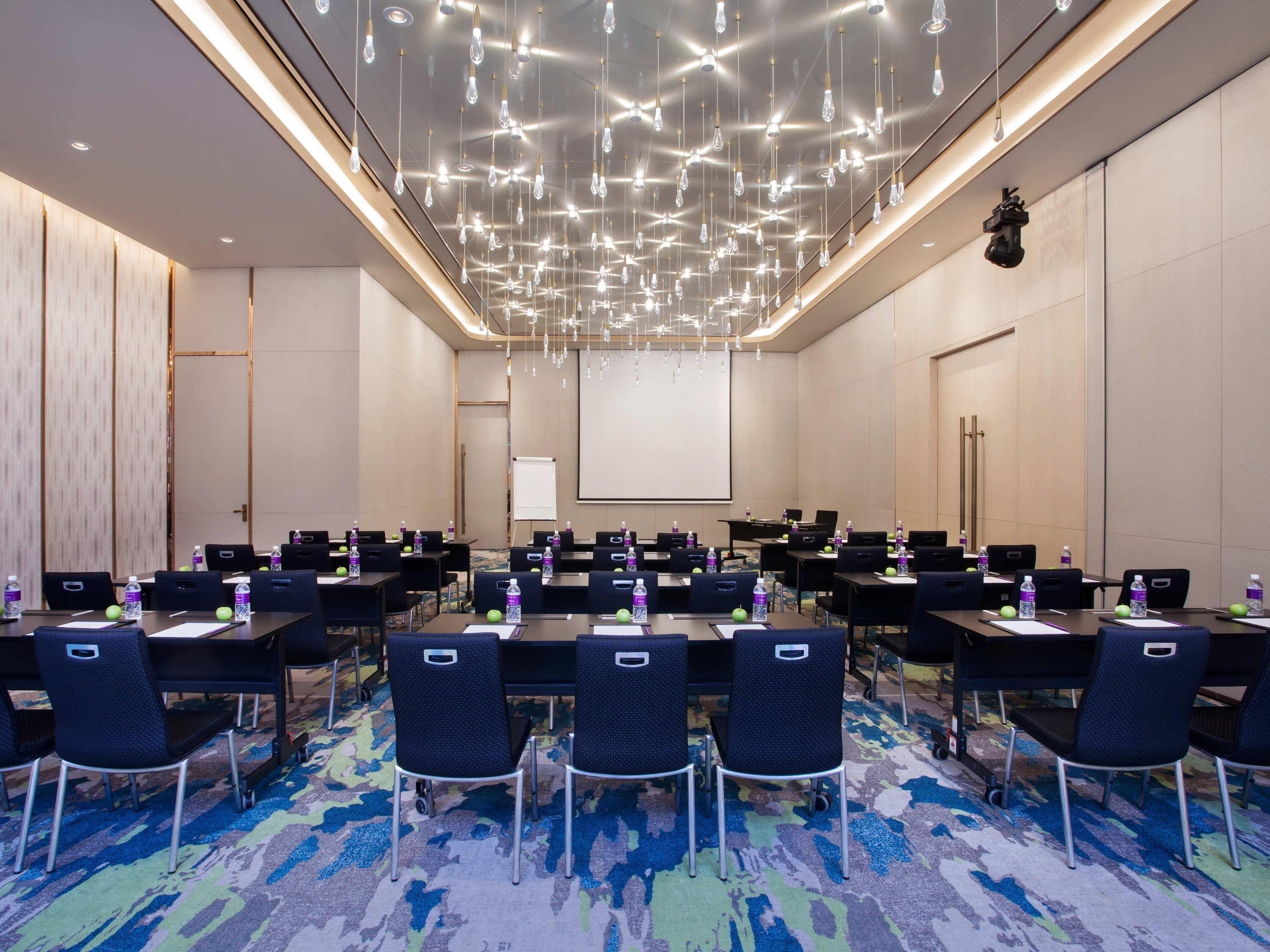 Une salle de conférence équipée de tables, de chaises, d’ordinateurs portables, de bouteilles d’eau et d’un écran de projection.