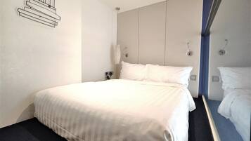 A hotel room with a large bed, a bedside table, a wall-mounted phone, and a mirror.