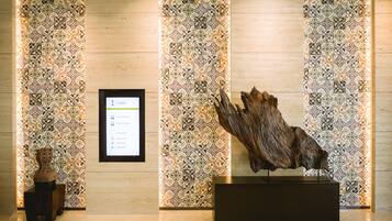 A lobby with patterned wallpaper, a reception desk, and a wooden sculpture on display.