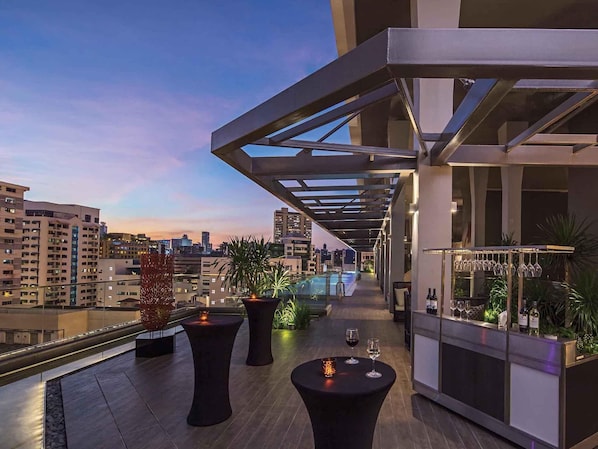 A rooftop terrace with a pool, tables, and potted plants.