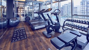 Un gimnasio moderno con equipo de ejercicio, ventanas amplias y vistas a la ciudad.