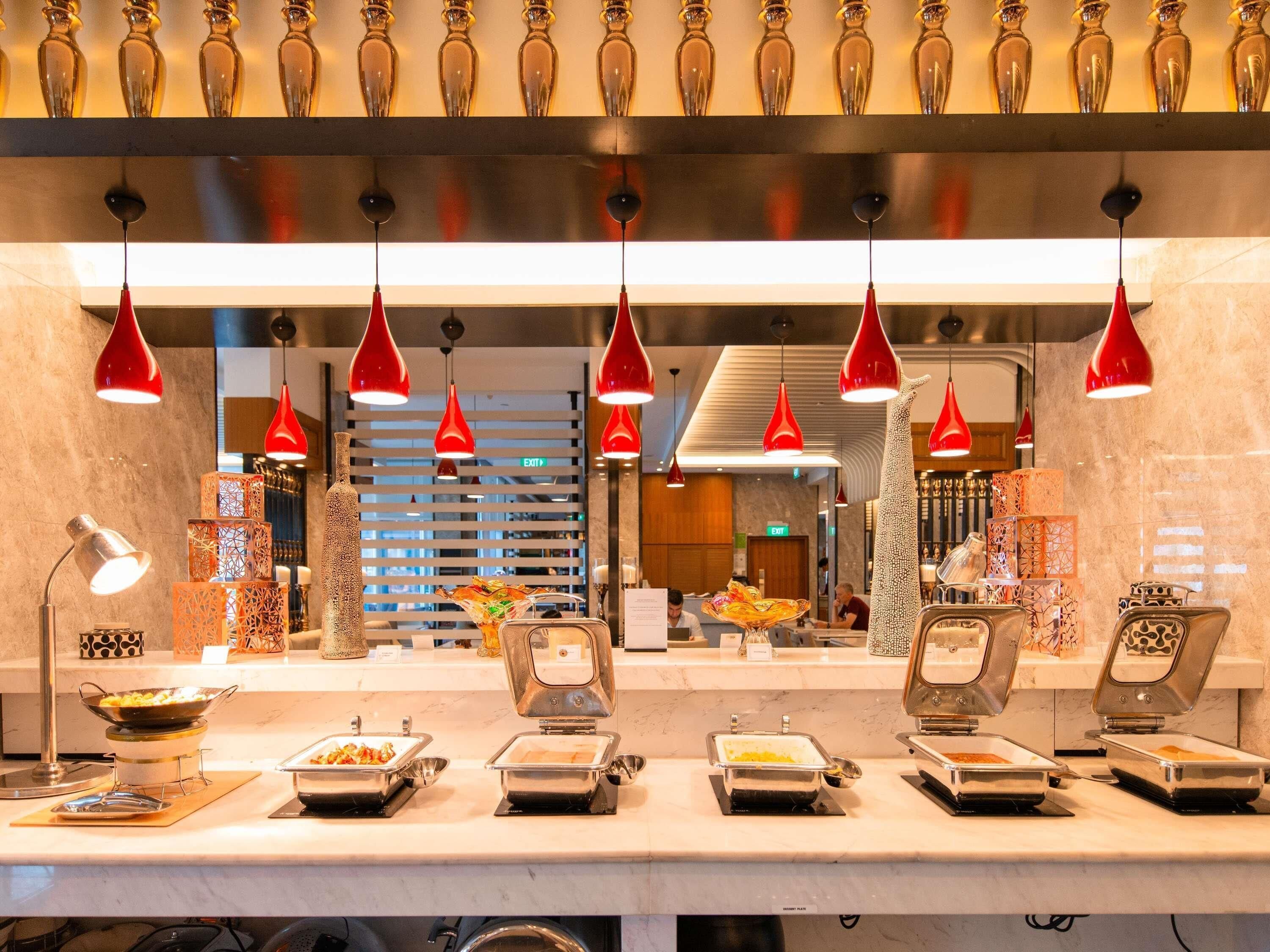 A buffet area with multiple food stations, overhead red pendant lighting, and a marble countertop.