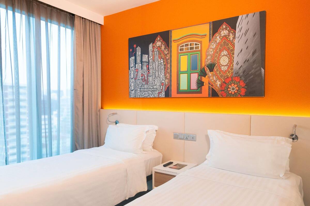 A hotel room with two beds, a large window with curtains, and a vibrant painting on the wall.