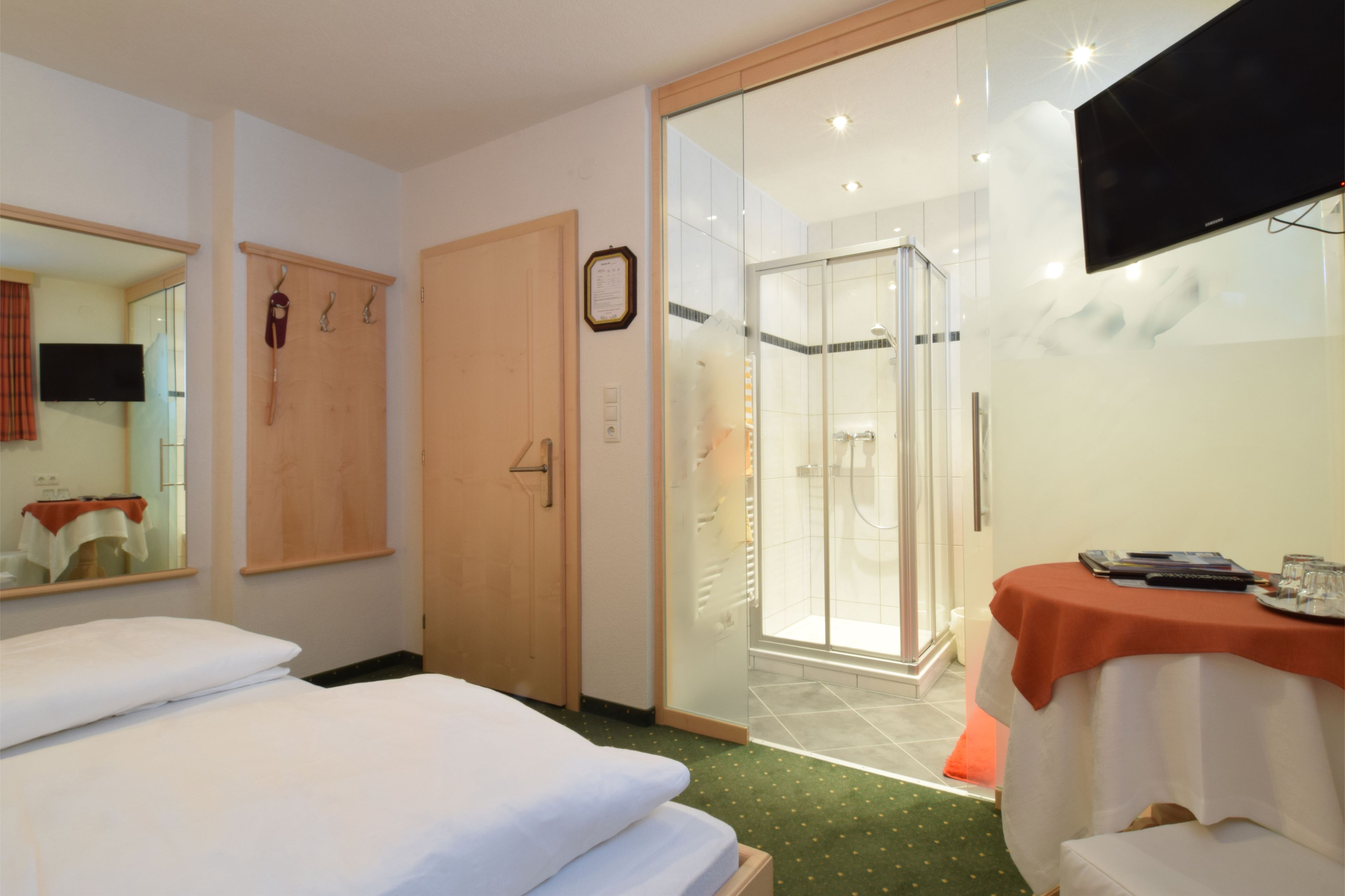 Habitación de hotel con dos camas, ducha, televisión y una mesa con mantel.