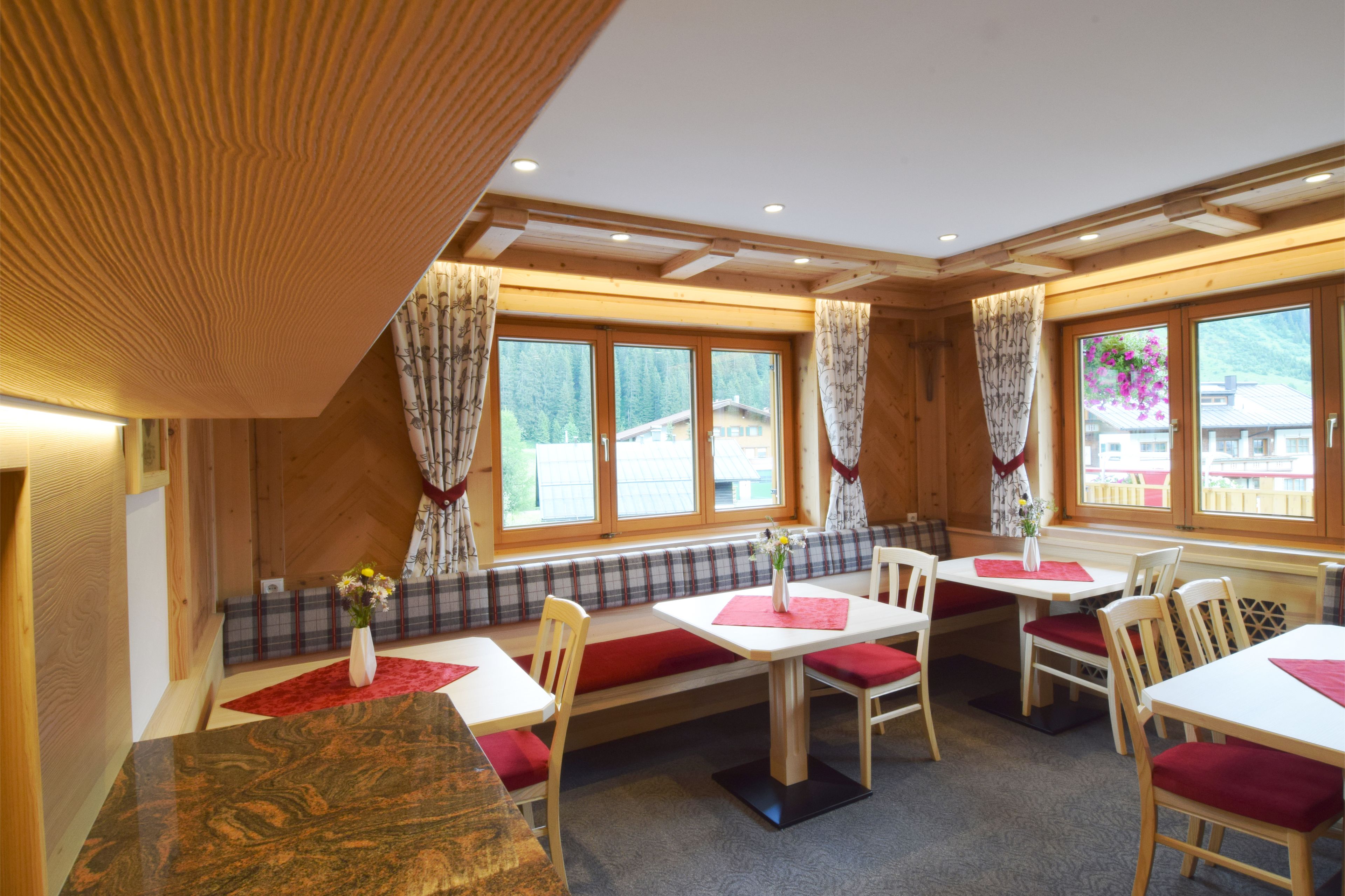 A dining area with wooden tables and benches, large windows with curtains, and a view of the outside.