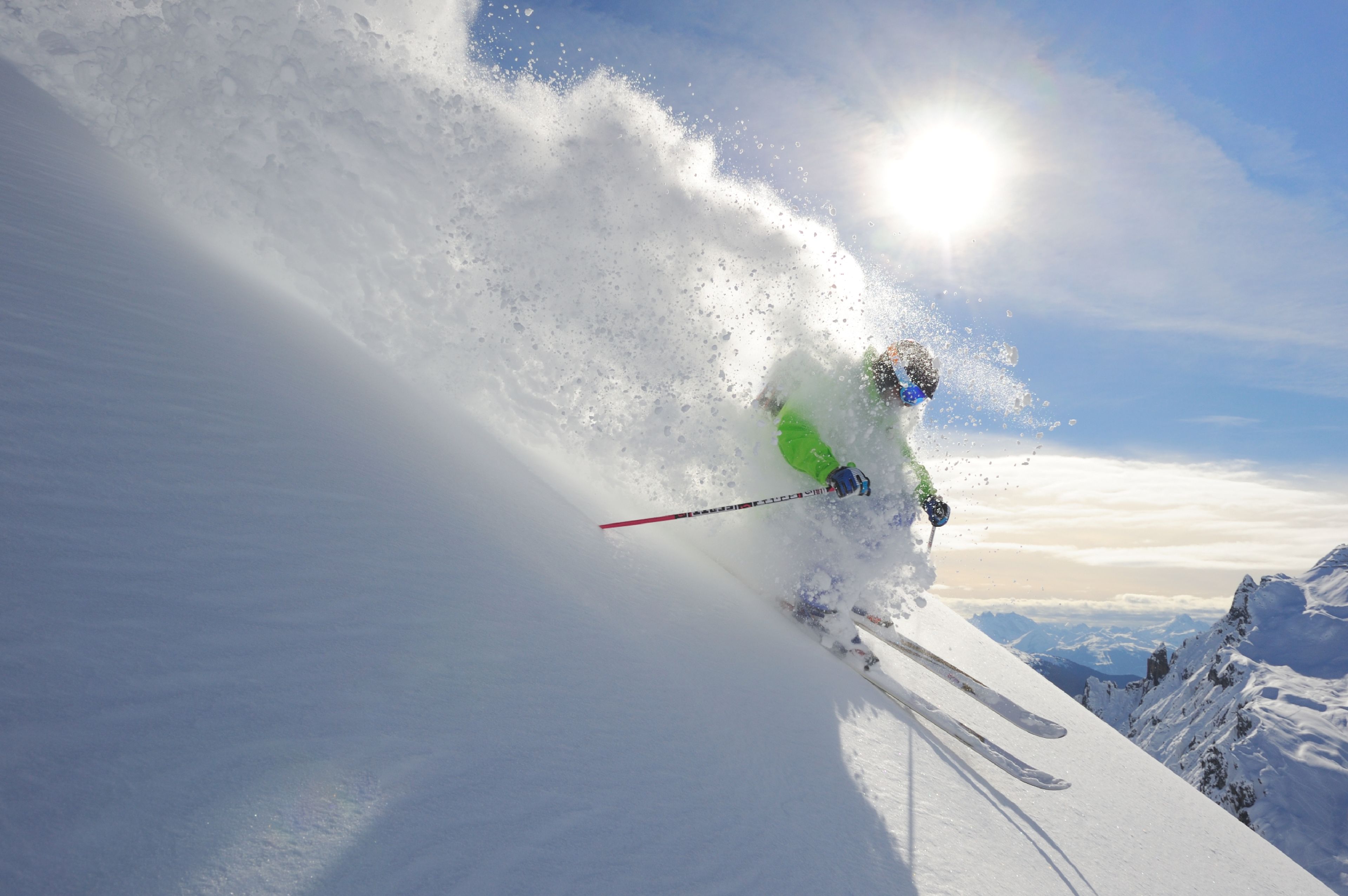 A skier in motion on a snowy slope with a clear sky and distant mountains.