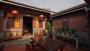 A traditional Chinese courtyard with a wooden table and benches, surrounded by potted plants and red lanterns. - Tomato Red (Jinsha)