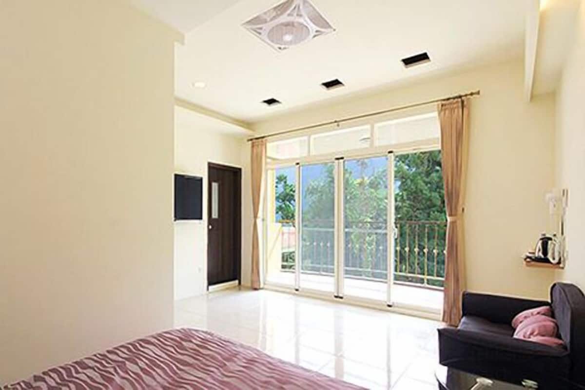 A bedroom with a bed, a sofa, a door, and a large sliding glass door leading to a balcony.