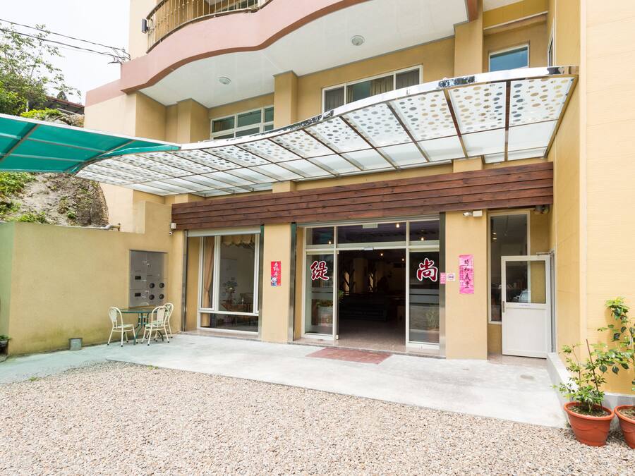 A hotel entrance with a covered patio area, a reception desk, and potted plants.