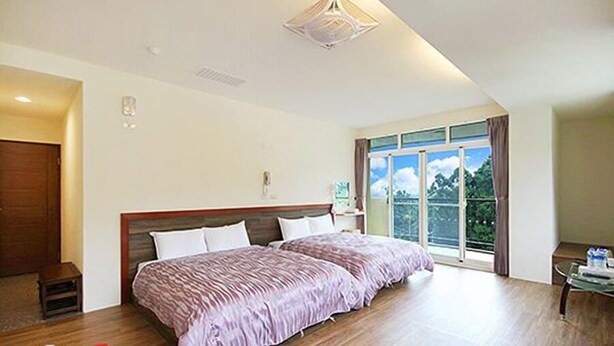 A bedroom with a large bed, a wooden floor, a ceiling light fixture, and a window with a view of greenery. - Shangti (Lugu)