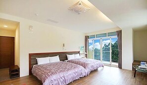 Un dormitorio con una cama grande, piso de madera, lámpara de techo y ventana con vista a follaje.