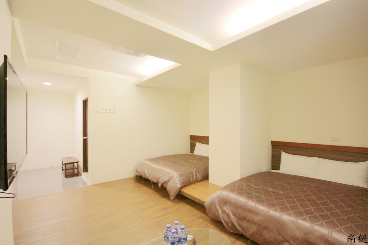 A hotel room with two beds, a small table with water bottles, and a TV.