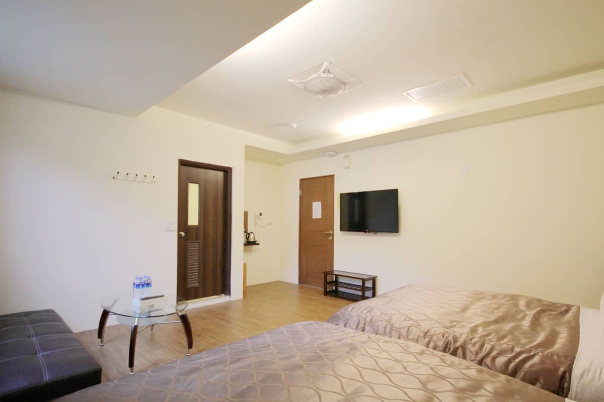 A hotel room with two beds, a TV, a small table, and a door leading to another room.