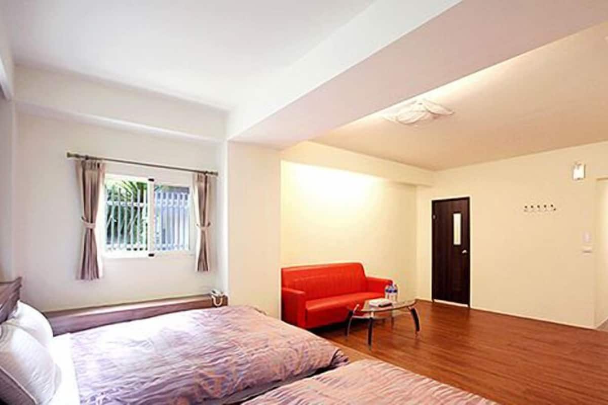 A hotel room with a bed, a red sofa, a small table, and a door.