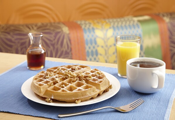 A breakfast setting with a waffle, a cup of coffee, and a glass of orange juice on a table with a blue placemat.