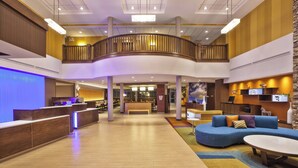 Eine geräumige Lobby mit einer Rezeption, einem geschwungenen Holzbalkon, einem blauen Sofa und einem kleinen Tisch.
