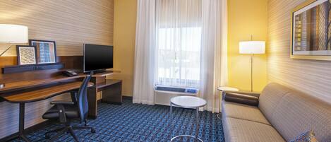 A hotel room with a desk, chair, television, sofa, and a patterned carpet.