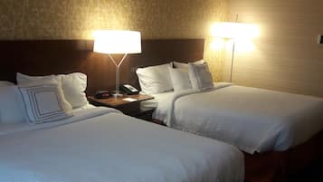 Camera d'albergo con due letti, un comodino con una lampada e una parete decorata.