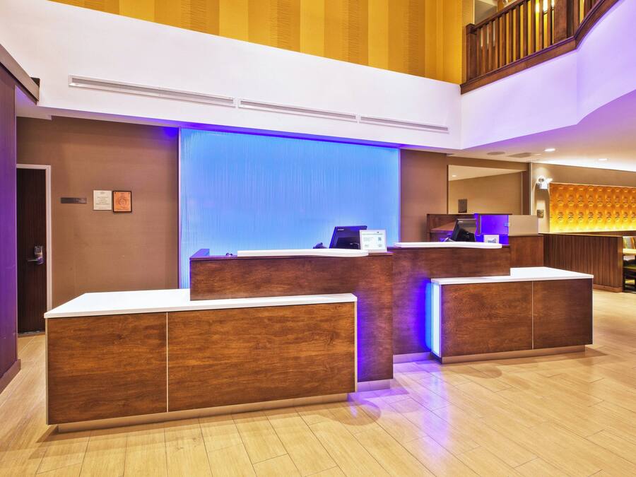 A hotel reception area with a wooden reception desk, a blue accent wall, and a staircase in the background.