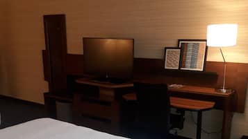Et hotelværelse med en seng, et skrivebord, et fjernsyn og en lampe.