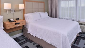 A hotel room with a large bed, a nightstand with a phone and a lamp, and a window with curtains.