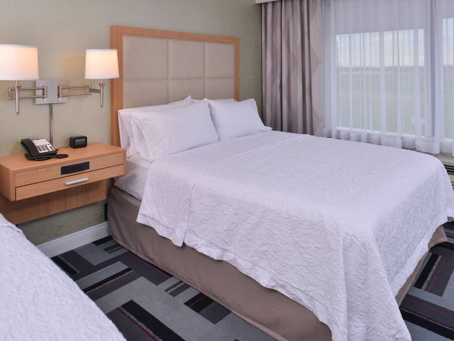 A hotel room with a large bed, a nightstand with a phone and a lamp, and a window with curtains.