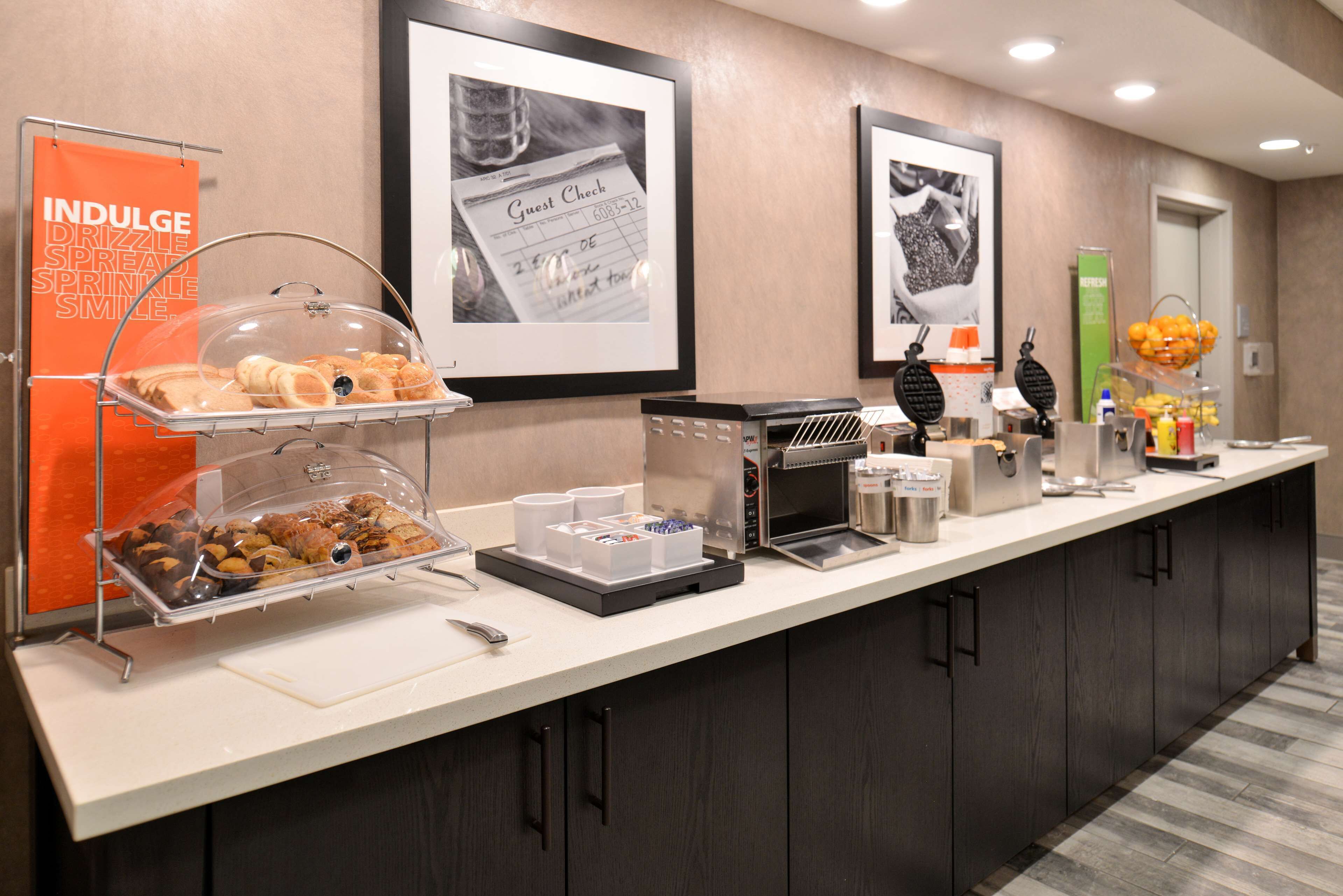 A hotel breakfast bar with a variety of pastries, a coffee machine, and a guest check-in area.