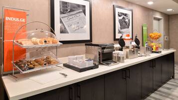 A hotel breakfast bar with a variety of pastries, a coffee machine, and a guest check-in area.